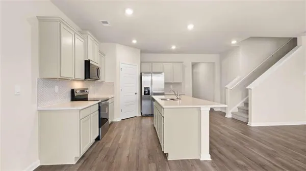 a kitchen with a sink a refrigerator a stove and white cabinets with wooden floor