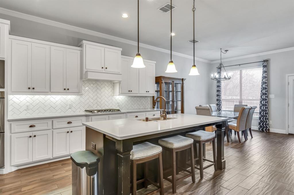 1306 Elizabeth Street Anna, TX 75409 - Photo 26 of 36 Kitchen with white cabinetry, crown molding, hanging light fixtures, a breakfast bar area, and backsplash