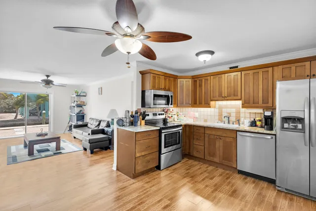 a kitchen with stainless steel appliances granite countertop a stove top oven a refrigerator a sink dishwasher a dining table and chairs with wooden floor