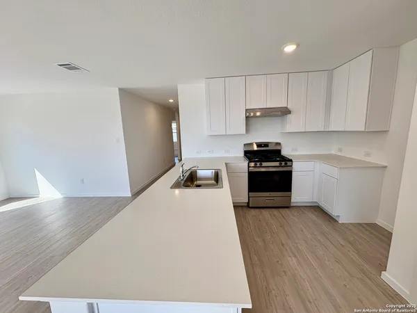 a kitchen with granite countertop a refrigerator a stove a sink and white cabinets with wooden floor