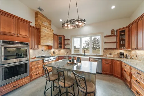 a kitchen with stainless steel appliances granite countertop a stove top oven a sink dishwasher a dining table and chairs with wooden floor