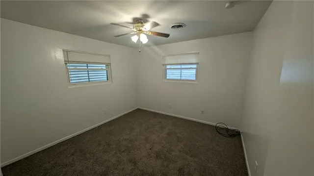 an empty room with a chandelier fan and windows