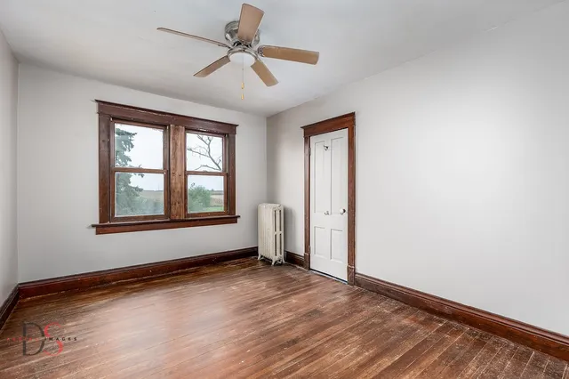 an empty room with wooden floor chandelier fan and windows