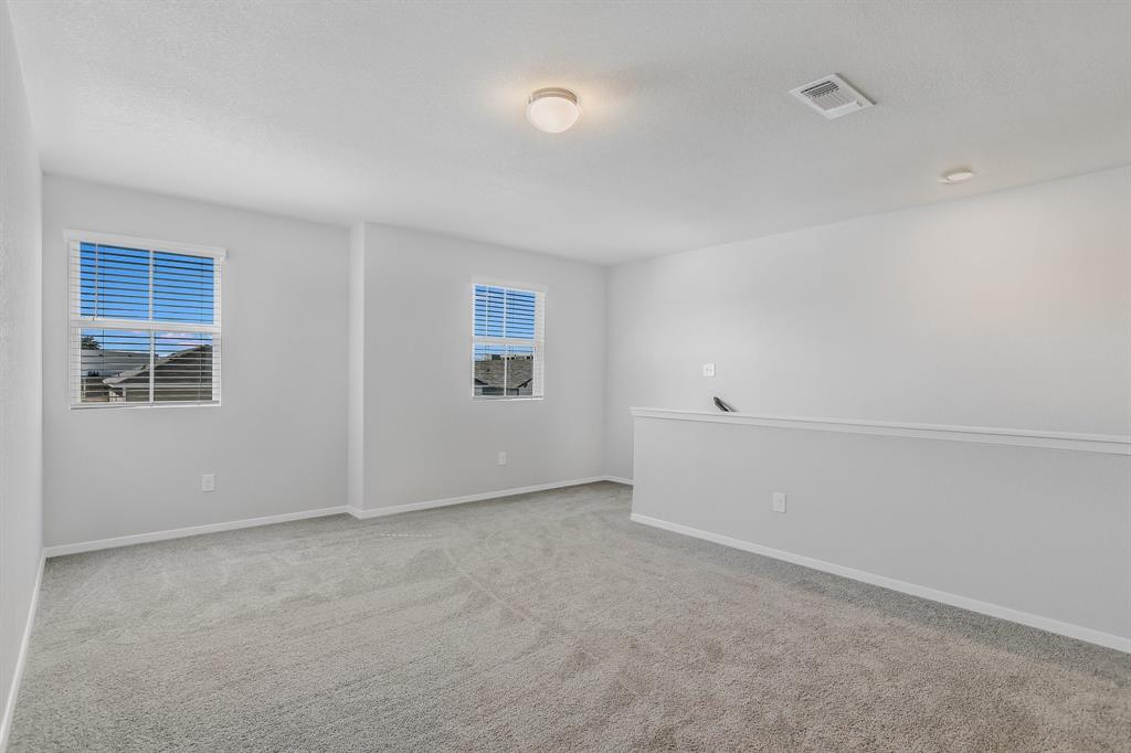 2808 Totley Road Manor, TX 78653 - Photo 13 of 21 Open concept room featuring two windows with horizontal blinds, neutral carpet flooring, and a low partial wall
