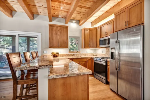 a kitchen with stainless steel appliances granite countertop a wooden cabinets a refrigerator a stove a sink and a dining table with wooden floor