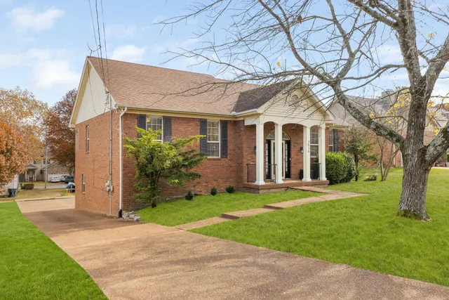 a view of a white house next to a yard with big trees
