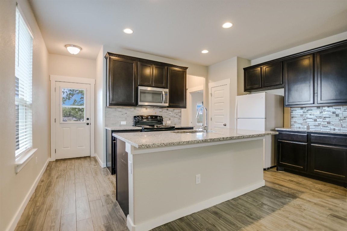 124 Ancellotta Way Leander, TX 78641 - Photo 9 of 20 Kitchen featuring stainless steel microwave, black electric range, freestanding refrigerator, decorative backsplash, and light stone countertops