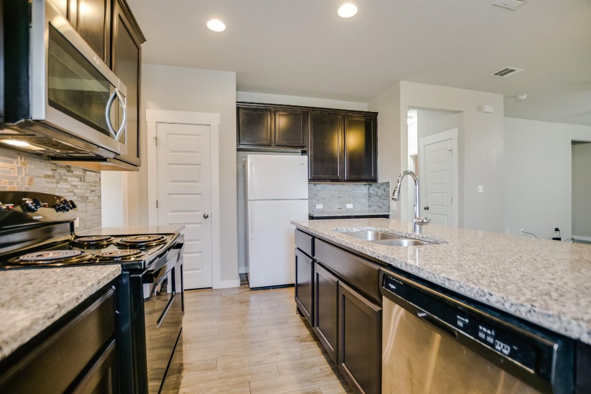124 Ancellotta Way Leander, TX 78641 - Photo 10 of 20 Kitchen with appliances with stainless steel finishes, backsplash, light stone counters, dark brown cabinetry, and light wood finished floors