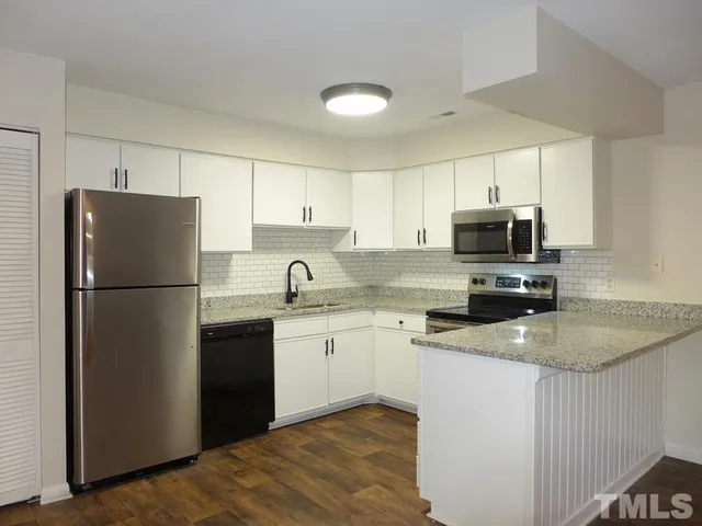 a kitchen with stainless steel appliances granite countertop a refrigerator a sink a stove a microwave and white cabinets