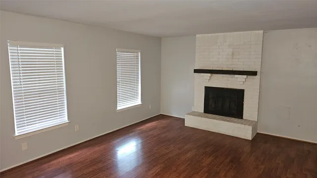 an empty room with wooden floor a fireplace and windows