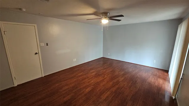 an empty room with wooden floor fan and windows