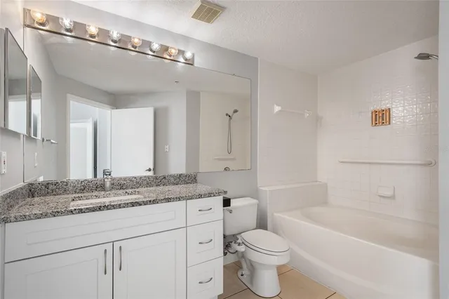a bathroom with a granite countertop sink a toilet a mirror and bathtub