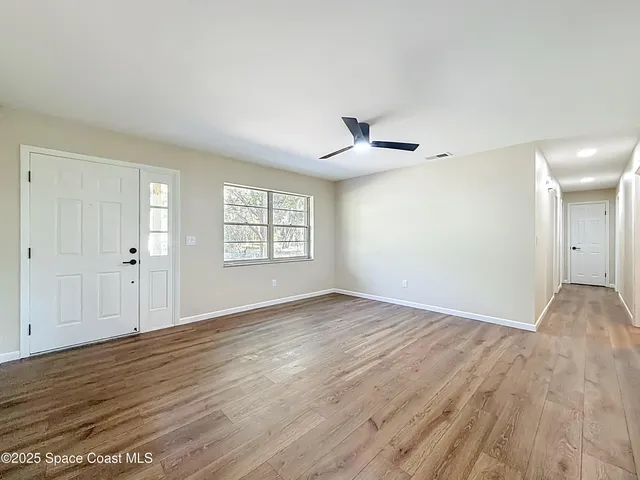 an empty room with wooden floor ceiling fan and windows