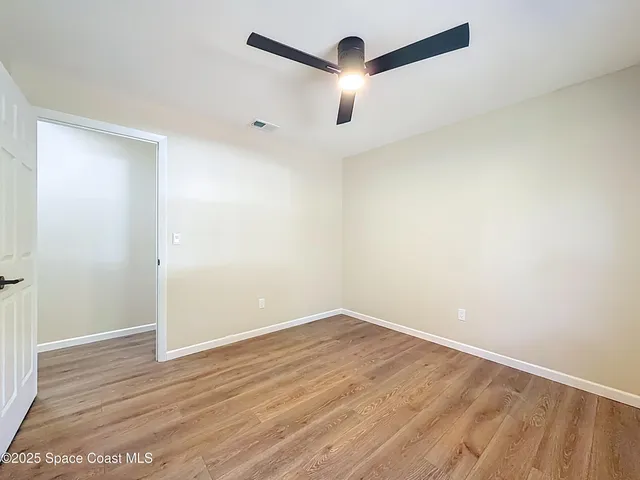 an empty room with wooden floor fan and windows
