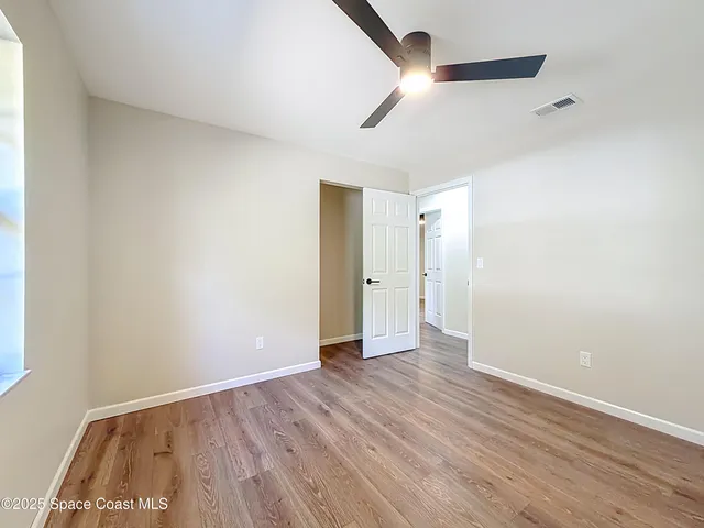an empty room with wooden floor ceiling fan and windows