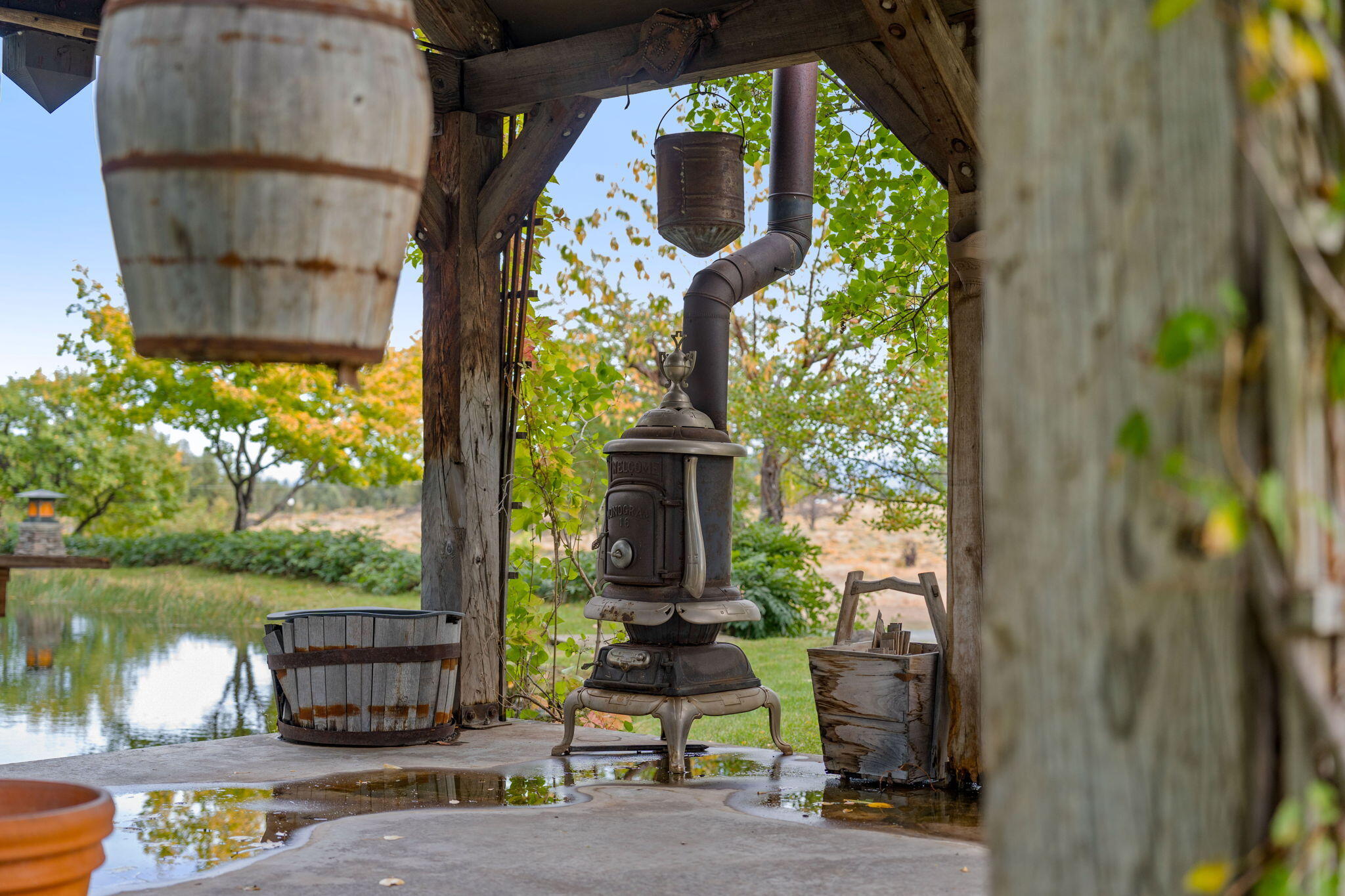 21925 Bear Creek Road Bend, OR 97702 - Photo 62 of 104 Old pot bellied stove on the concrete patio of the gazebo built with salvaged timber from an old Bend barn. Lots of hanging baskets, planter barrels and antiques