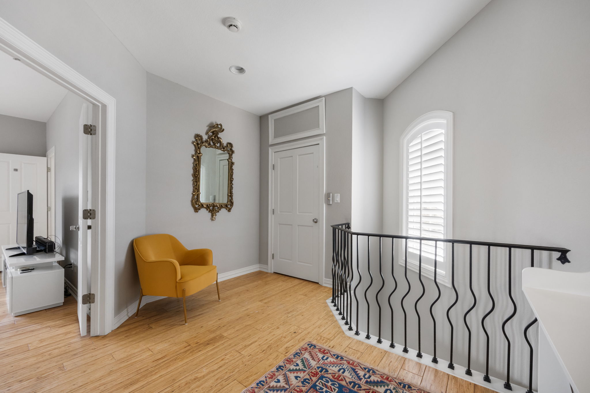 1910 Rue De St Tropez, Unit 6 Austin, TX 78746 - Photo 22 of 37 A graceful staircase with intricate ironwork leads to an upper landing with hardwood flooring and an arched window.