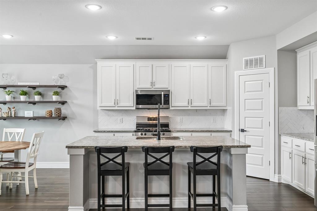 1805 Huntsman Way Forney, TX 75126 - Photo 6 of 34 Kitchen featuring a central island with countertop seating, white shaker cabinetry, stainless steel appliances, and wood-finish flooring