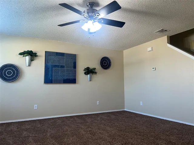 an empty room with a ceiling fan and kitchen view