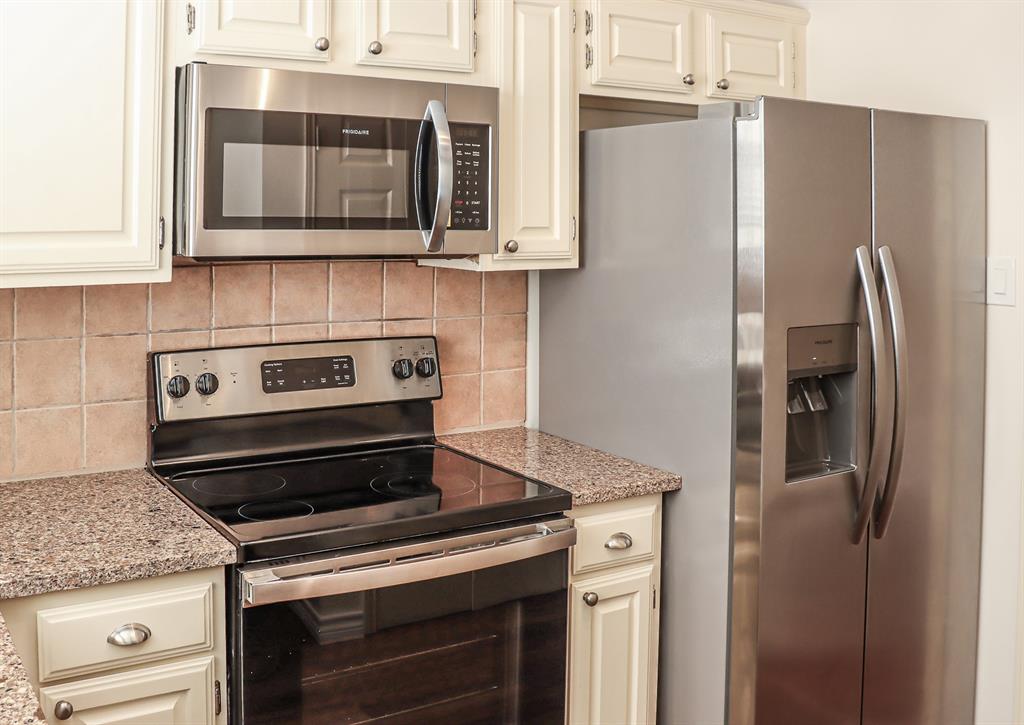 5565 Preston Oaks Road, Unit 120 Dallas, TX 75254 - Photo 4 of 27 Updated kitchen featuring cream-colored cabinetry, granite countertops, stainless steel appliances including a side-by-side refrigerator with ice and water dispensers, electric range with cooktop, and overhead microwave.