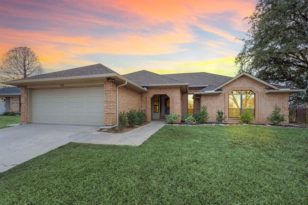 Ranch-style home with a shingled roof, a garage, driveway, a front lawn, and brick siding