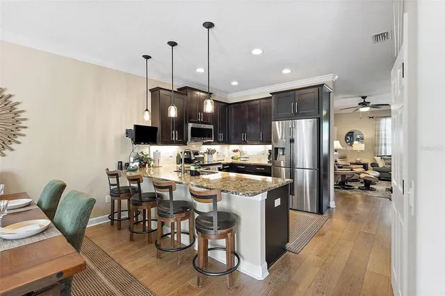 a kitchen with stainless steel appliances kitchen island granite countertop a refrigerator a stove a dining table and chairs with wooden floor