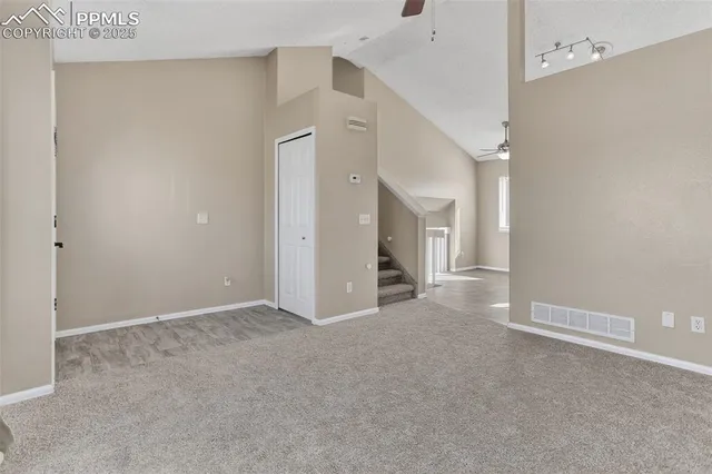 a view of an empty room with wooden floor and a chandelier fan