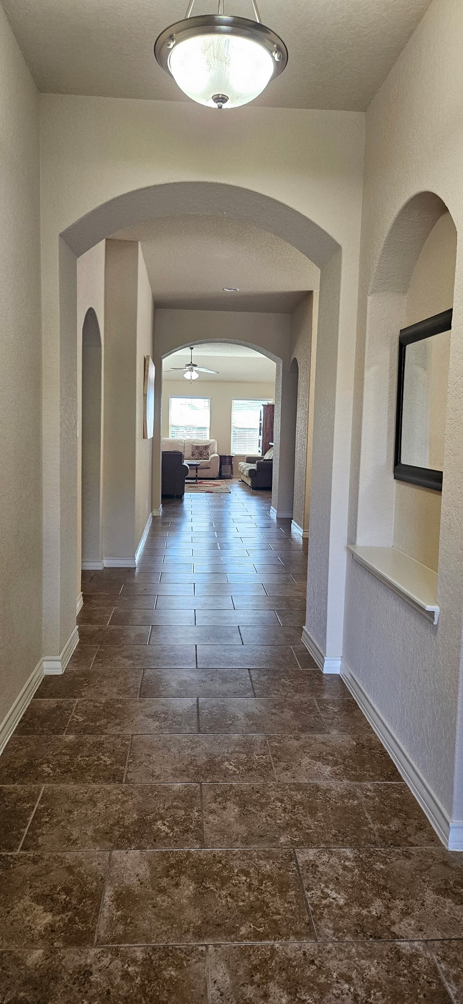 449 Cactus Flower Cibolo, TX 78108 - Photo 2 of 19 This photo showcases a long, elegant hallway with arched doorways and tile flooring, leading to a bright living area with ample natural light.