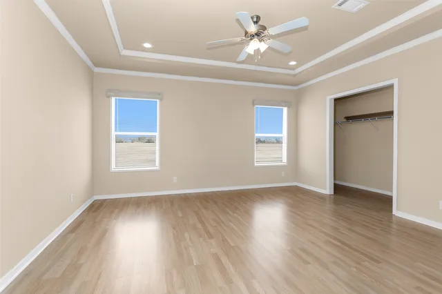 an empty room with wooden floor ceiling fan and windows