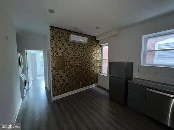 a view of a refrigerator in kitchen and an empty room with wooden floor