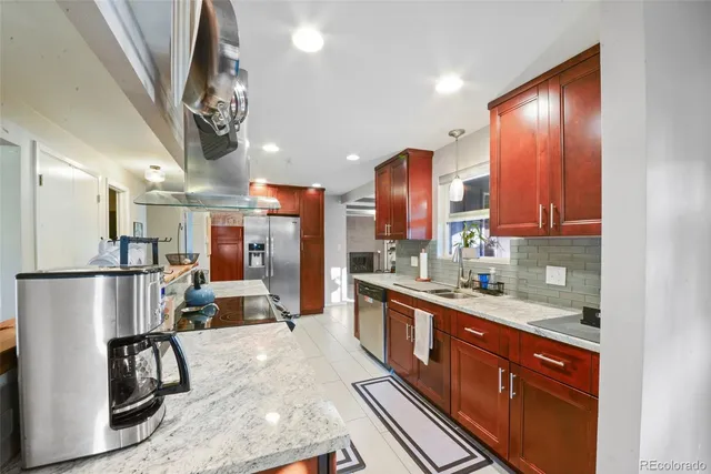 a kitchen with stainless steel appliances granite countertop a refrigerator a sink dishwasher a stove and a dining table with wooden floor