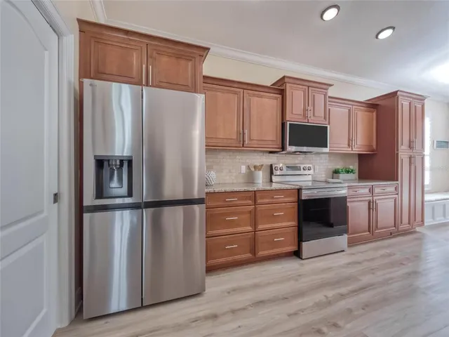 a large kitchen with stainless steel appliances granite countertop a refrigerator a sink dishwasher a oven and a dining table with wooden floor