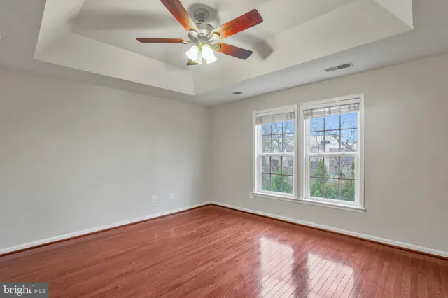 an empty room with wooden floor chandelier fan and windows