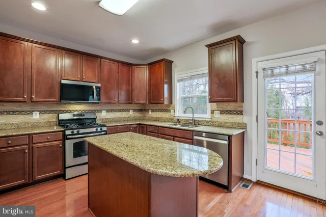a kitchen with stainless steel appliances granite countertop wooden cabinets a stove top oven a sink and dishwasher with wooden floor