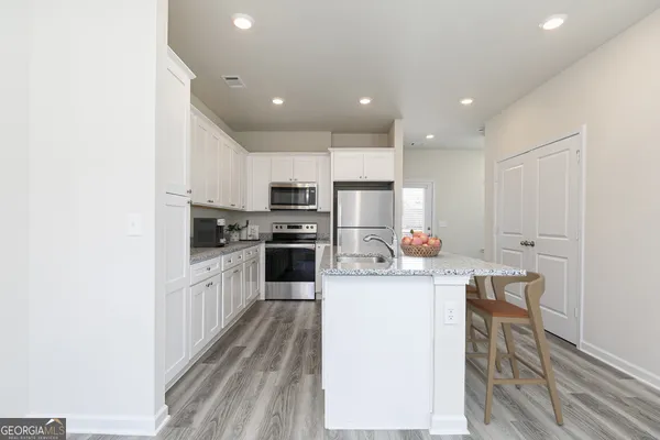 a kitchen with stainless steel appliances a microwave a stove a sink dishwasher and white cabinets with wooden floor