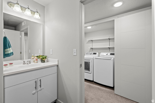 64 West 600 South, Unit C205 Springville, UT 84663 - Photo 17 of 23 Convenient laundry room with side-by-side washer and dryer, white cabinetry with ample storage, recessed lighting, and direct access to the adjoining bathroom featuring a vanity sink, chrome fixtures, and mirror with integrated lighting