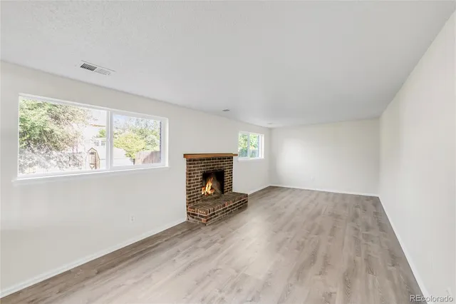 an empty room with windows a fireplace and wooden floor