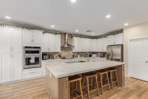 a large kitchen with kitchen island a stove a sink a refrigerator and white cabinets with wooden floor