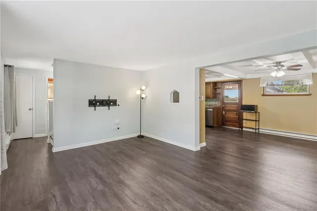 an empty room with wooden floor and way to kitchen