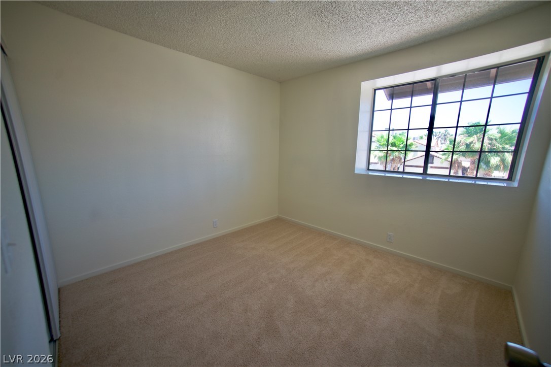 6501 Hartwood Road Las Vegas, NV 89108 - Photo 15 of 32 A well-lit bedroom features plush carpeting and a gridded window offering palm tree views.
