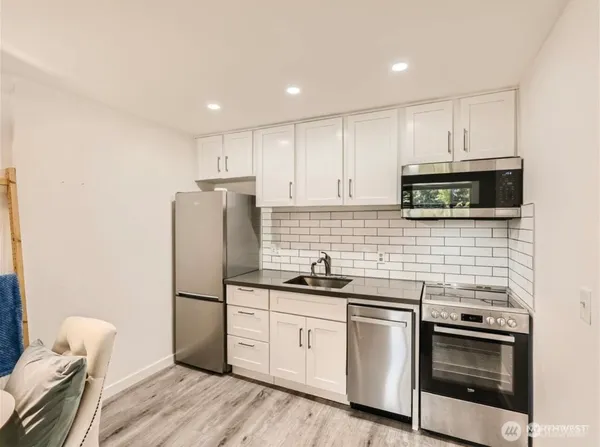 a kitchen with granite countertop white cabinets stainless steel appliances and a wooden floor