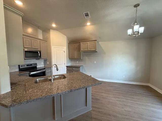 a kitchen with kitchen island granite countertop a sink a counter space appliances and cabinets