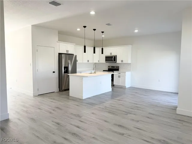 a kitchen with stainless steel appliances granite countertop a sink a stove a refrigerator and white cabinets with wooden floor