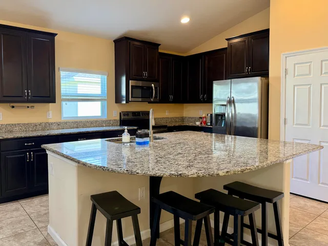 a kitchen with kitchen island granite countertop a table chairs microwave and refrigerator