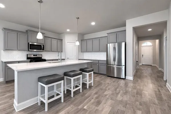 a kitchen with kitchen island granite countertop a refrigerator a stove a oven a sink a island with a chairs and wooden floor