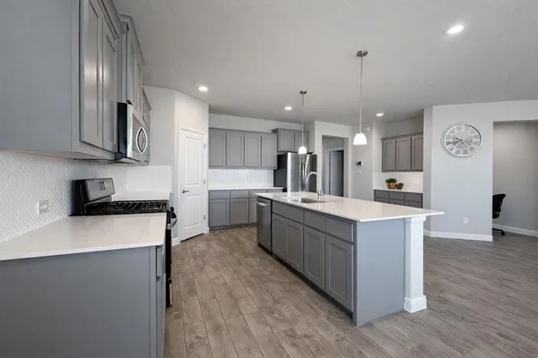 a large kitchen with stainless steel appliances kitchen island granite countertop a stove a sink a refrigerator and white cabinets with wooden floor