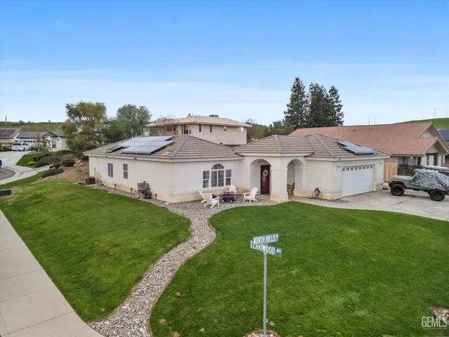 a white house with a big yard plants and large trees