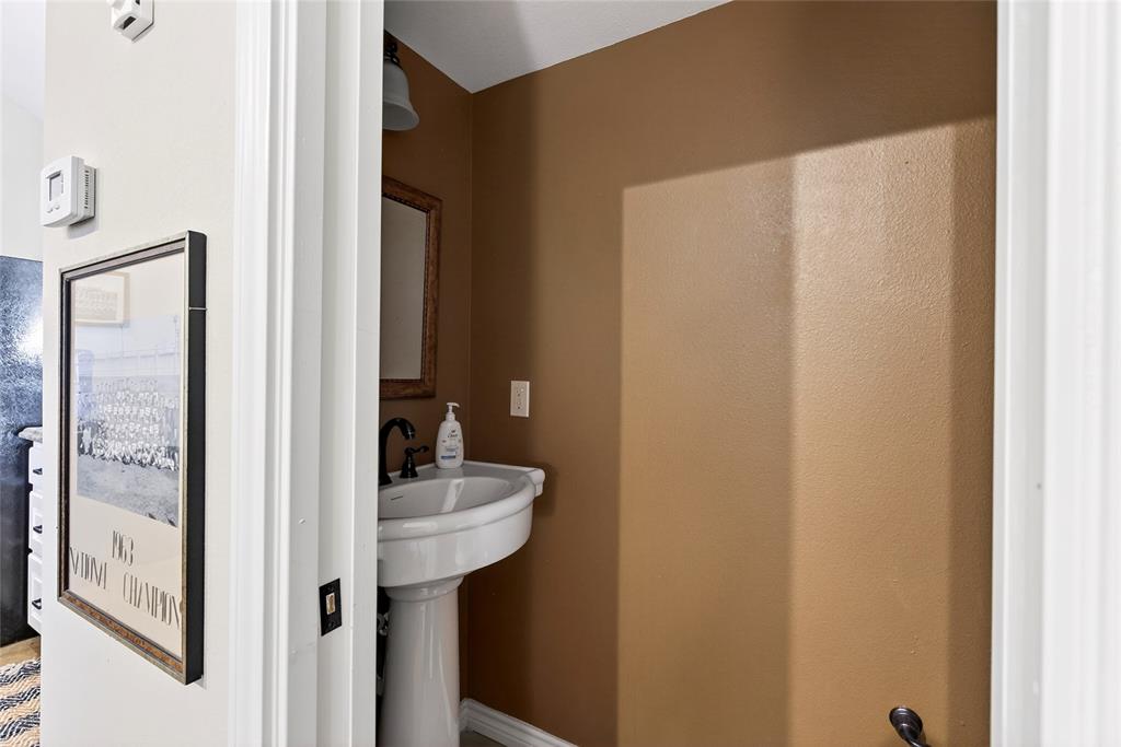 1113 Rim O The World Drive Tool, TX 75143 - Photo 28 of 40 Cabin 2nd Half Bath off of the living space features a pedestal sink with black faucet, complemented by a framed mirror and overhead lighting fixture, set against warm-toned walls.