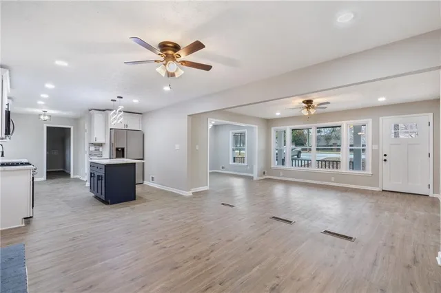 a view of an empty room with wooden floor and a kitchen