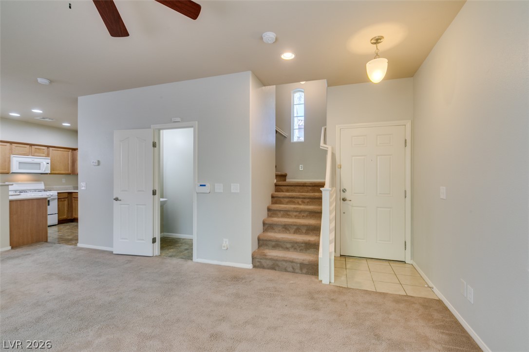 8937 Caledon Ridge Court Las Vegas, NV 89149 - Photo 10 of 43 A well-lit entryway leads to a carpeted living area and kitchen, featuring a staircase and main entrance.